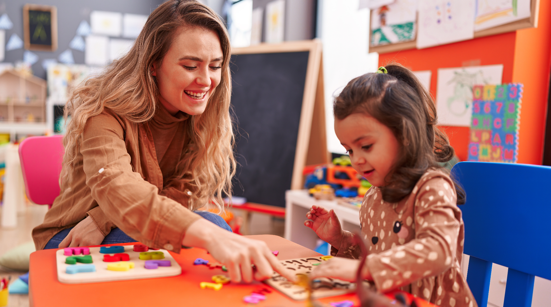 Teacher and toddler playing with a math puzzle game at a table in kindergarten